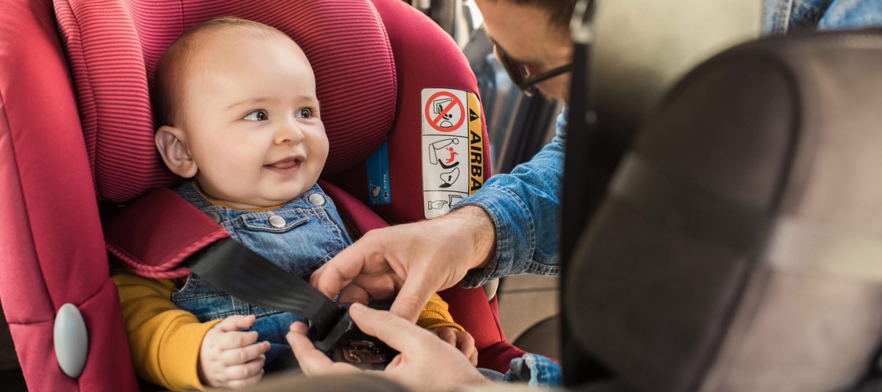 Father fasten his little baby in the car seat